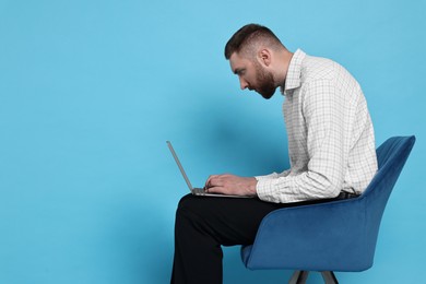Photo of Man with poor posture sitting on chair and using laptop against light blue background, space for text