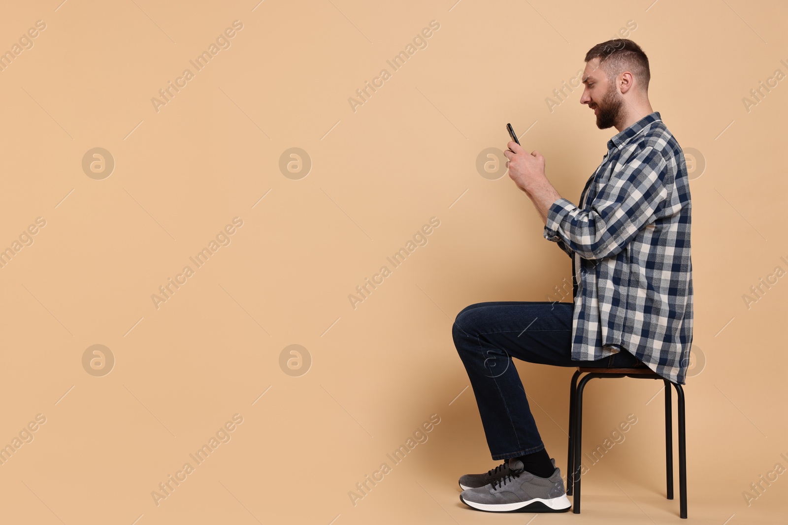 Photo of Man with good posture sitting on chair and using smartphone against pale orange background, space for text