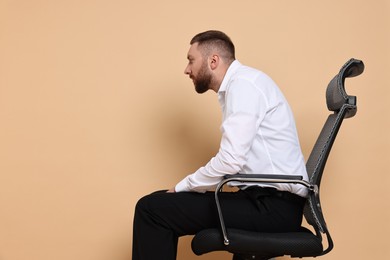 Man with poor posture sitting on chair against pale orange background, space for text