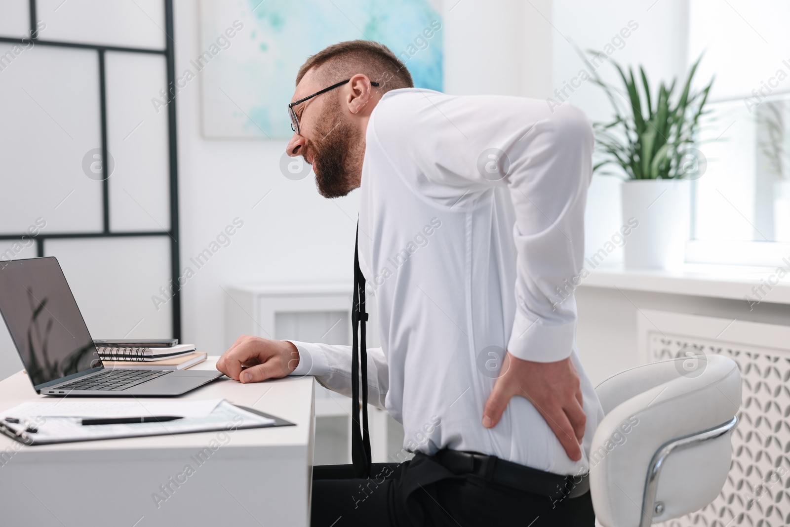 Photo of Man suffering from back pain in office. Symptom of poor posture