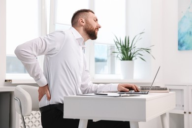 Photo of Man suffering from back pain in office. Symptom of poor posture