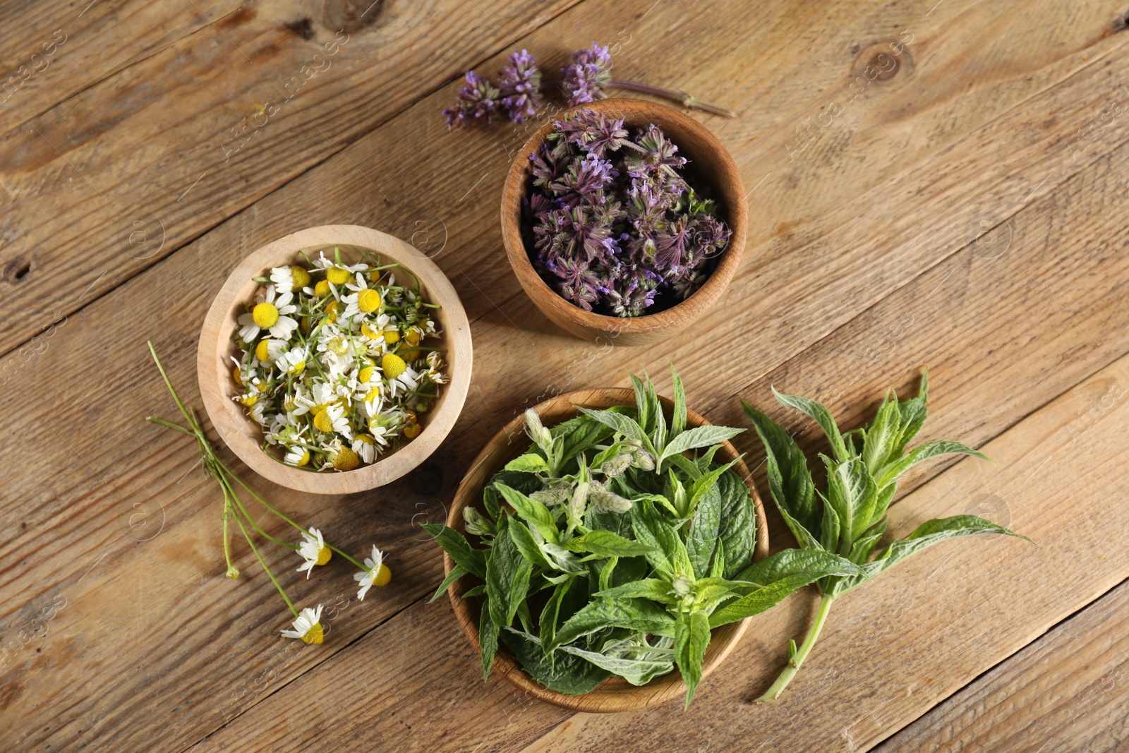 Photo of Different healing herbs in bowls on wooden table, flat lay