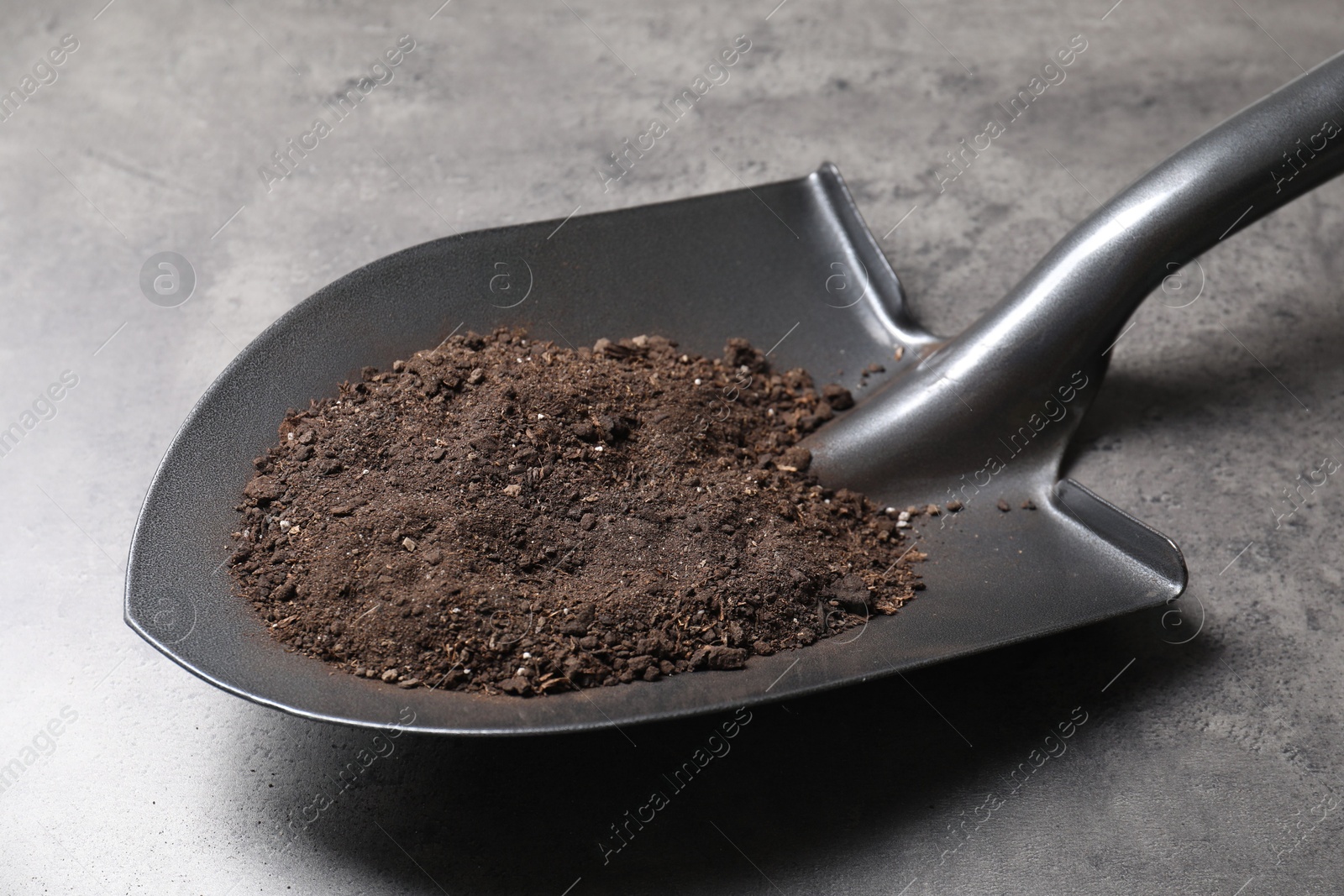 Photo of Metal shovel with soil on grey table, closeup