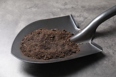 Photo of Metal shovel with soil on grey table, closeup