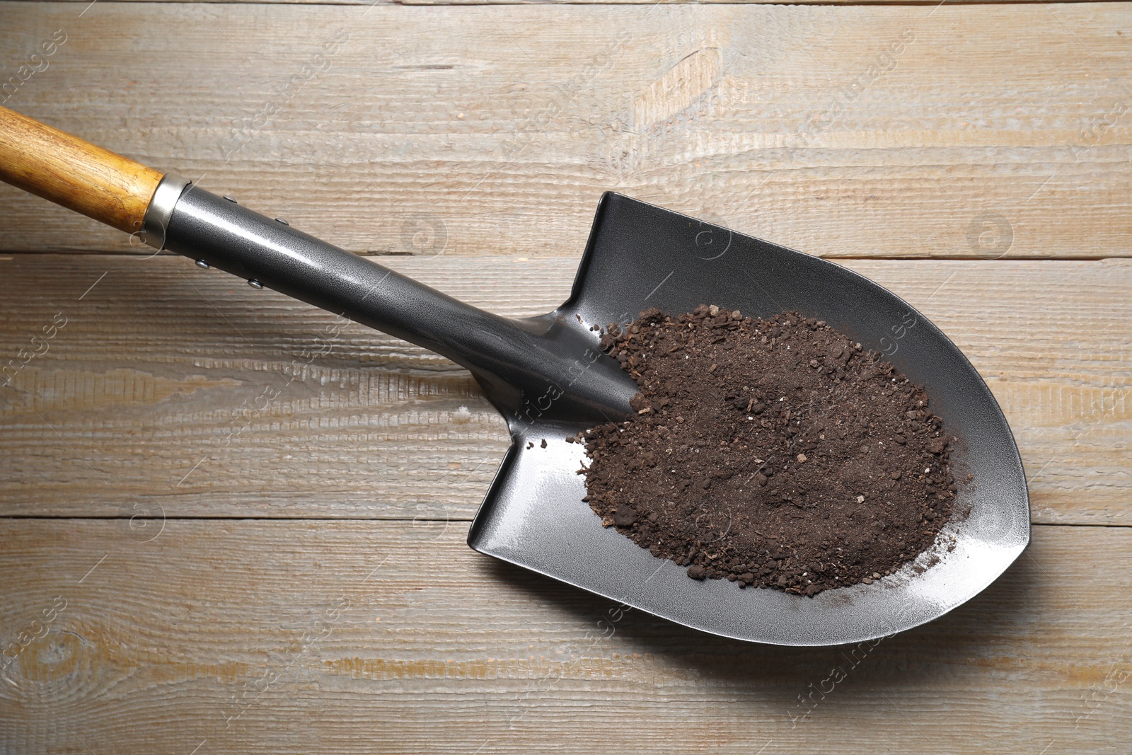 Photo of Metal shovel with soil on wooden table, top view