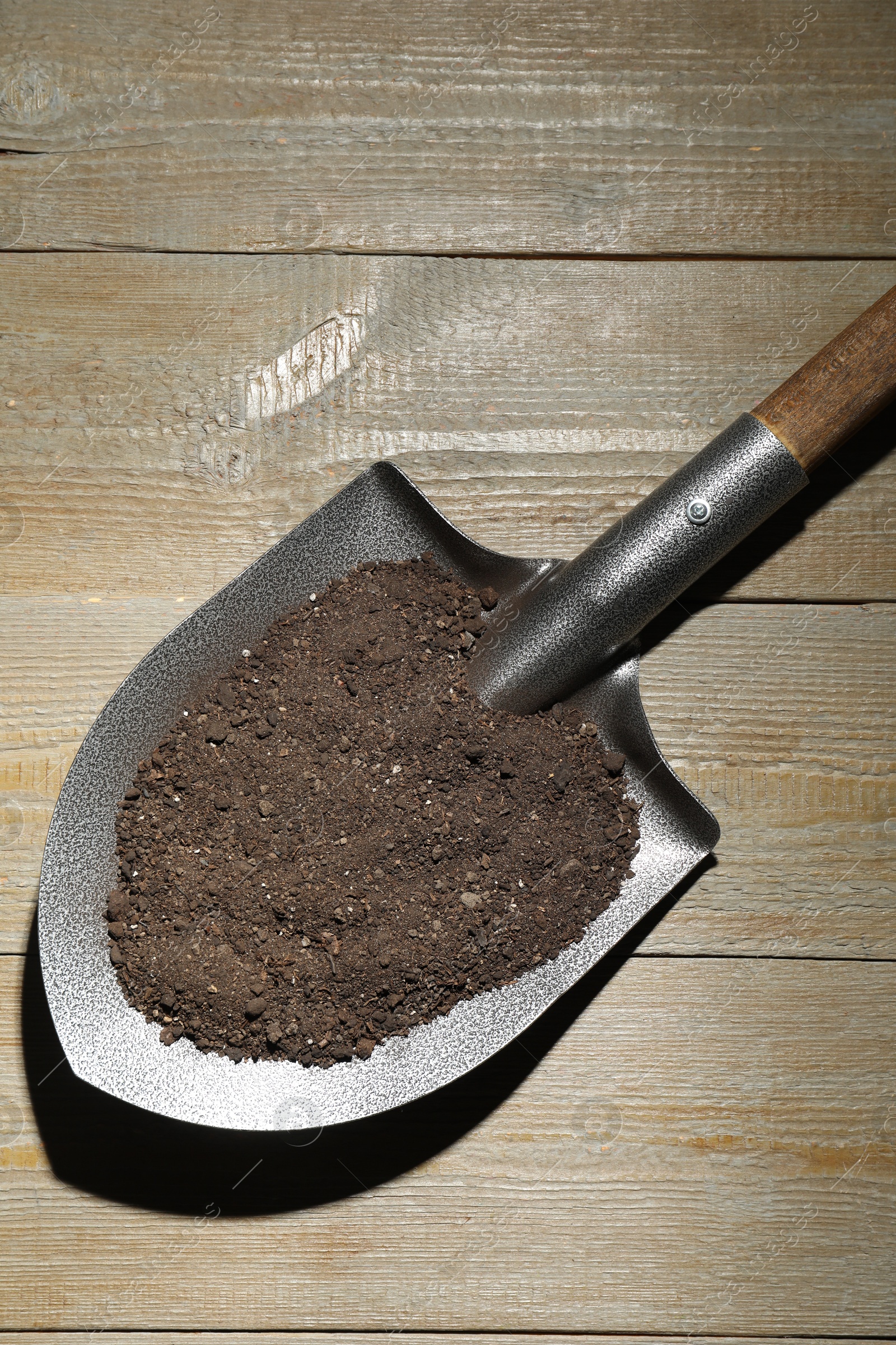 Photo of Metal shovel with soil on wooden table, top view