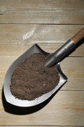 Photo of Metal shovel with soil on wooden table, top view