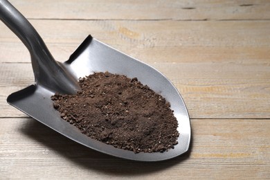 Photo of Metal shovel with soil on wooden table, closeup. Space for text