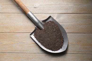 Photo of Metal shovel with soil on wooden table, top view