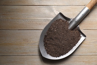 Photo of Metal shovel with soil on wooden table, top view. Space for text