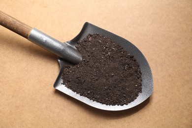 Photo of Metal shovel with soil on light brown table, top view