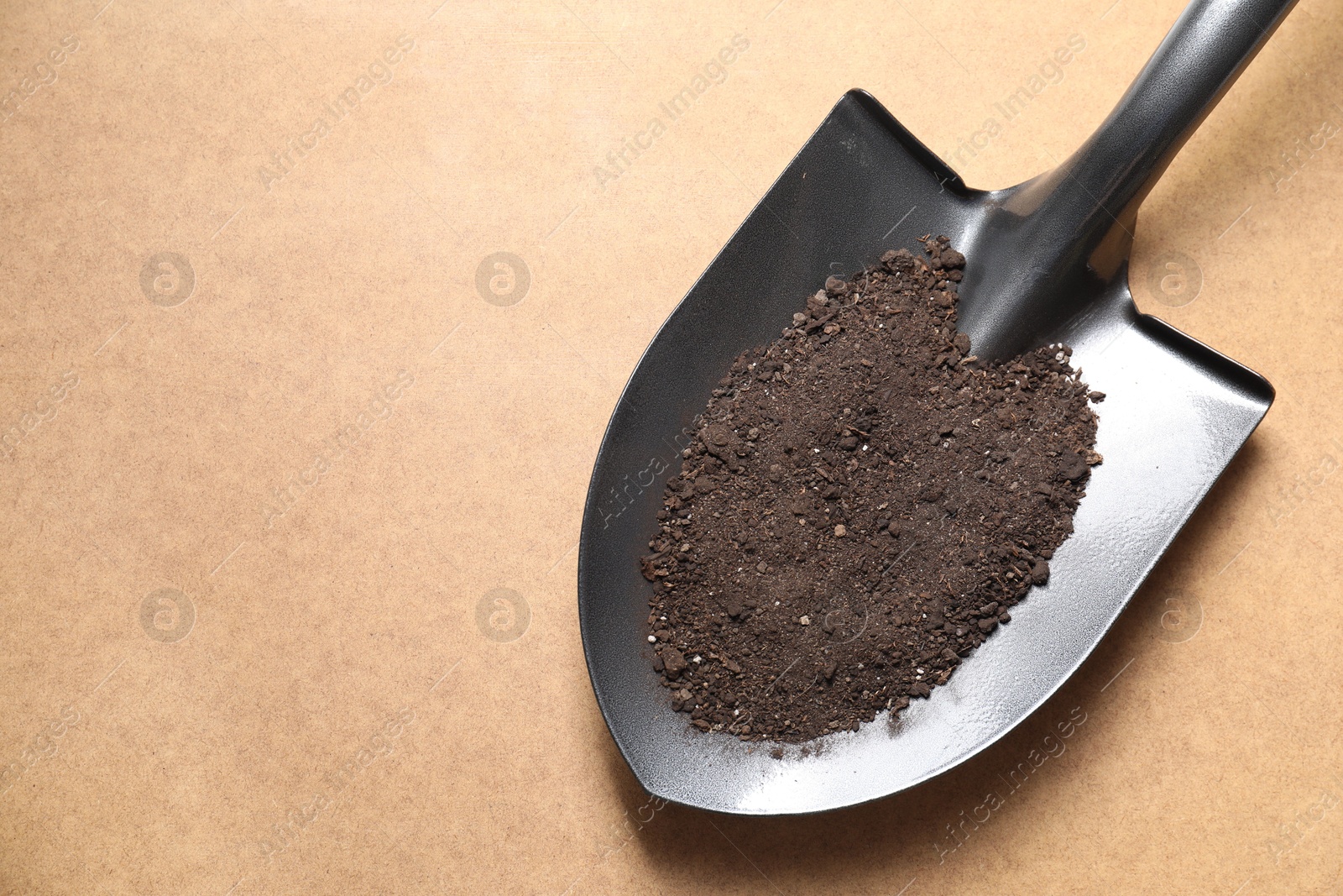 Photo of Metal shovel with soil on light brown table, top view. Space for text