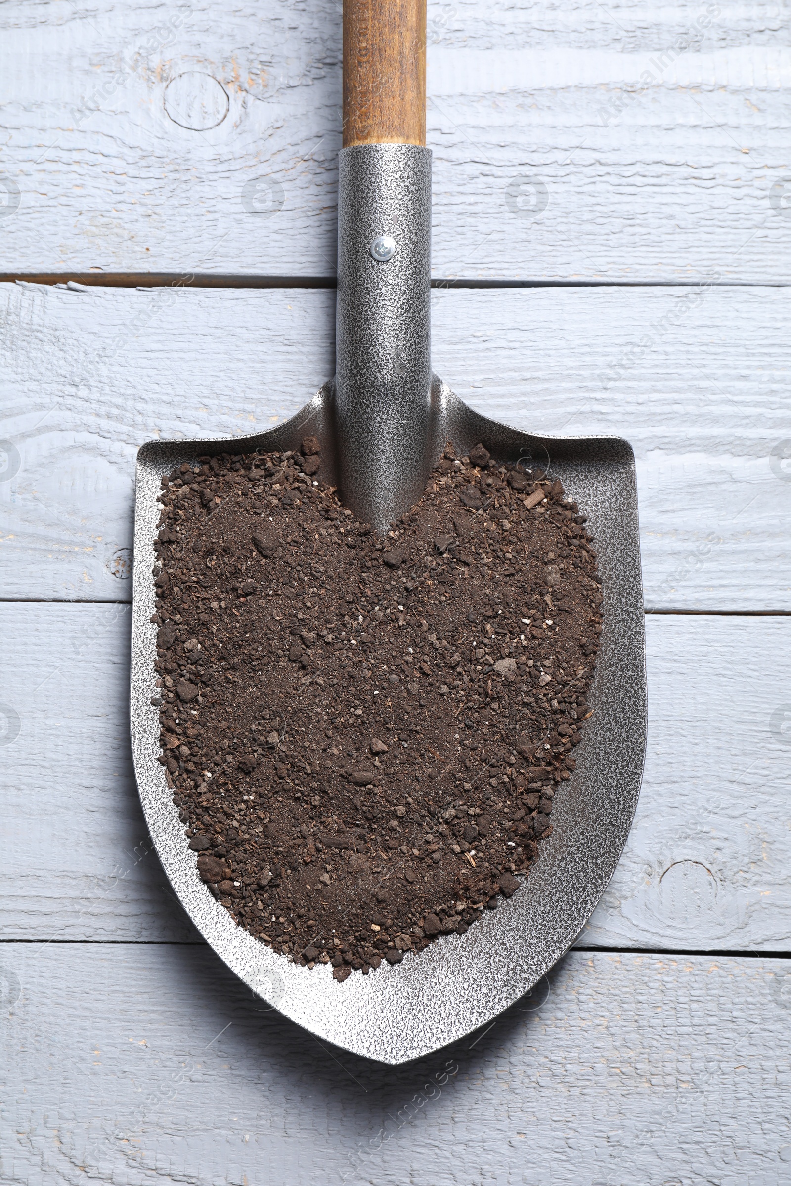 Photo of Metal shovel with soil on light grey wooden table, top view