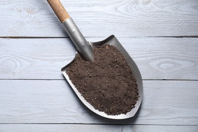 Photo of Metal shovel with soil on light grey wooden table, top view