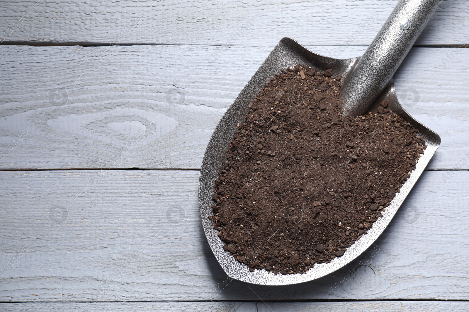 Photo of Metal shovel with soil on light grey wooden table, top view. Space for text