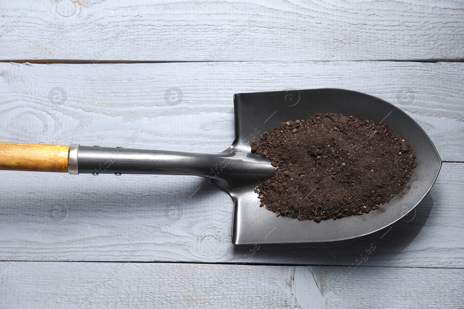 Photo of Metal shovel with soil on light grey wooden table, top view