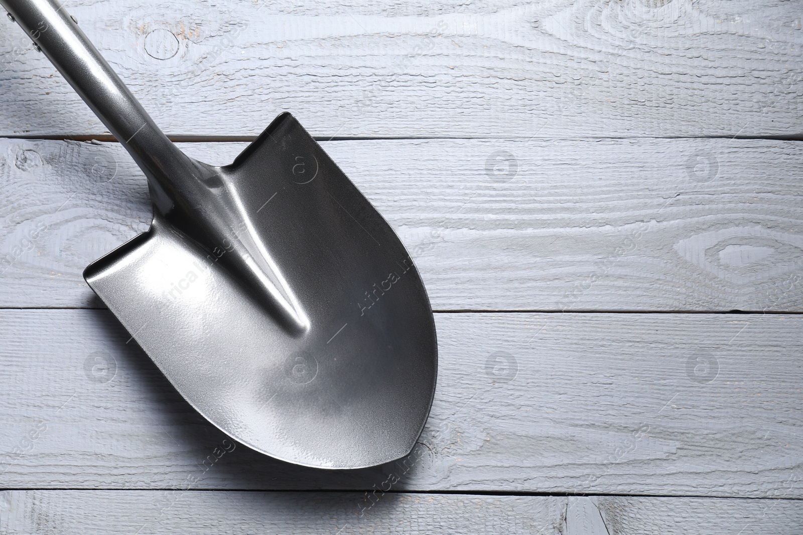 Photo of Metal shovel on light grey wooden table, top view. Space for text