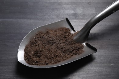 Photo of Metal shovel with soil on black wooden table, closeup