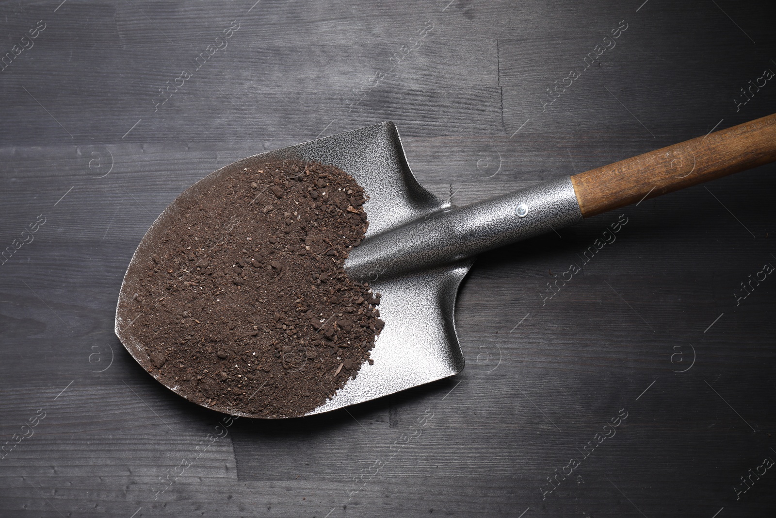 Photo of Metal shovel with soil on black wooden table, top view