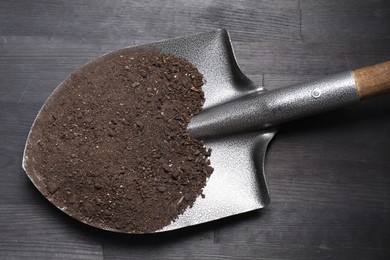 Photo of Metal shovel with soil on black wooden table, top view