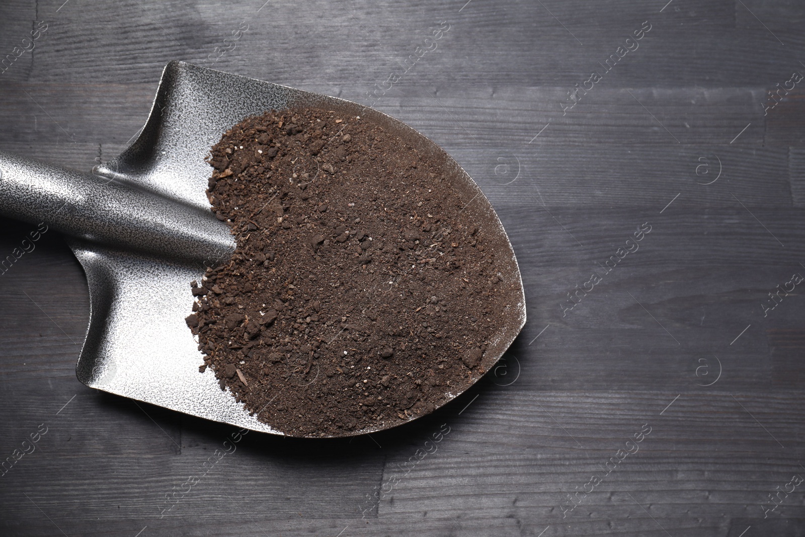 Photo of Metal shovel with soil on black wooden table, top view. Space for text