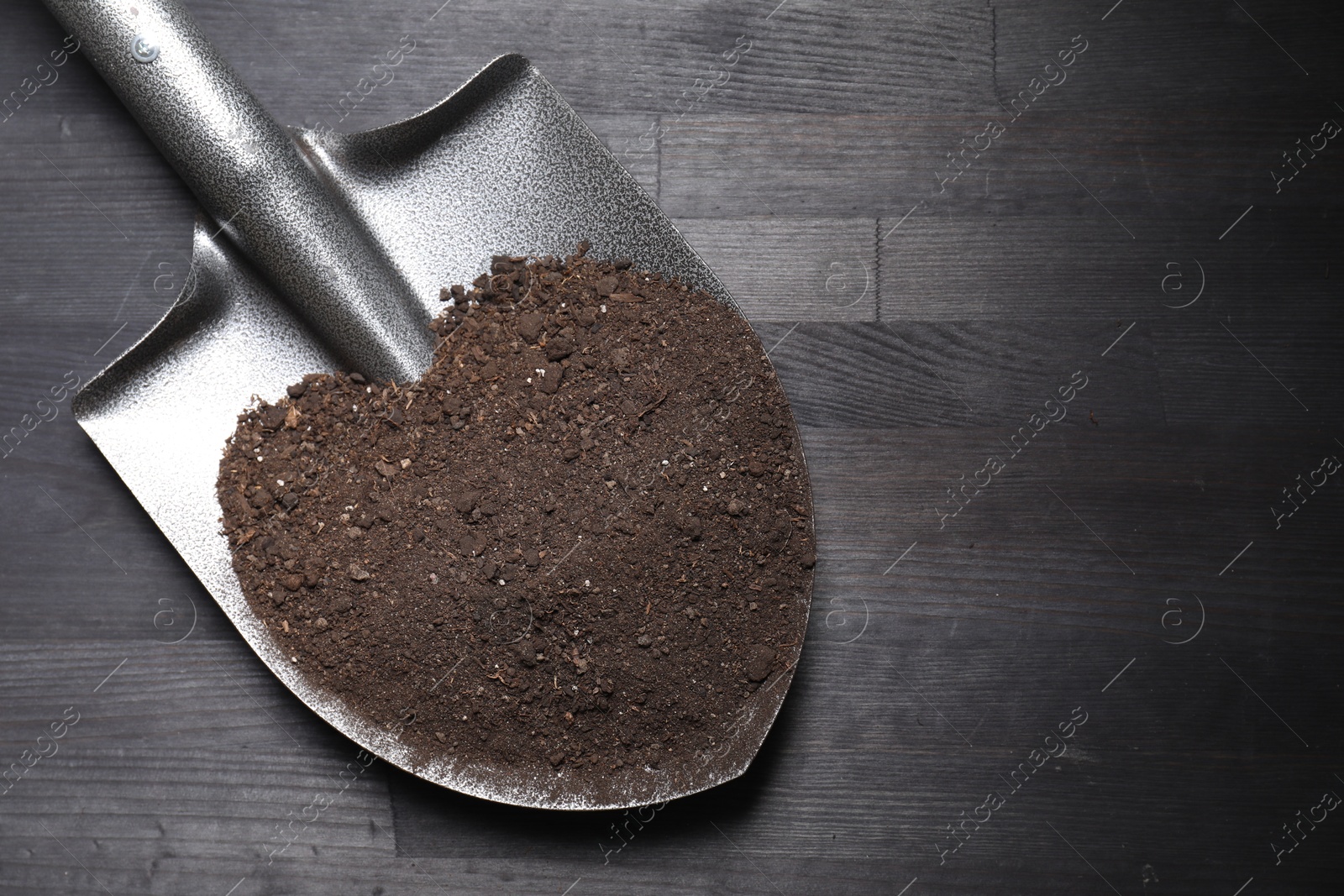 Photo of Metal shovel with soil on black wooden table, top view. Space for text