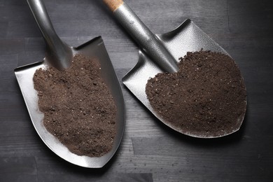 Photo of Metal shovels with soil on black wooden table, top view