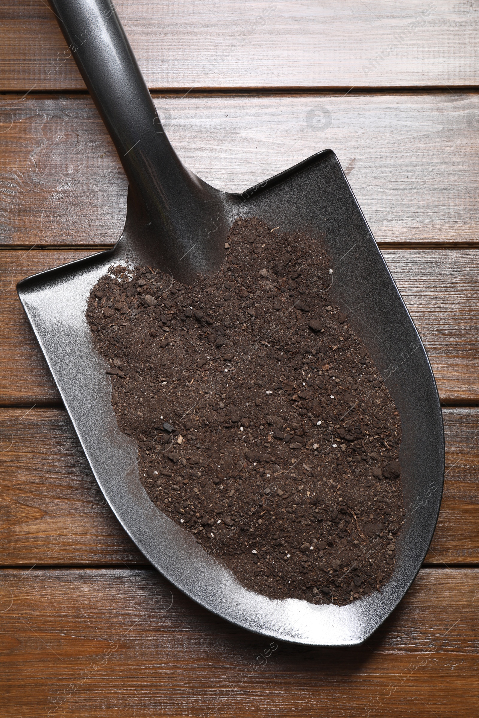 Photo of Metal shovel with soil on wooden table, top view