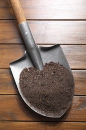 Photo of Metal shovel with soil on wooden table, top view