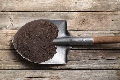 Photo of Metal shovel with soil on wooden table, top view