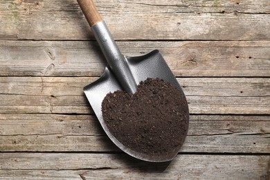 Photo of Metal shovel with soil on wooden table, top view