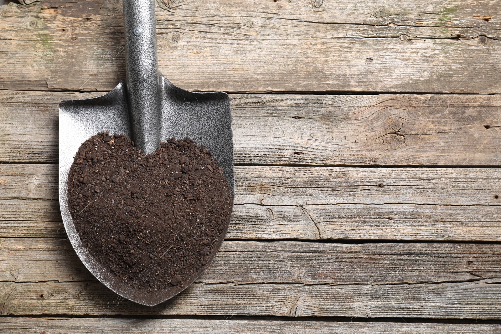 Photo of Metal shovel with soil on wooden table, top view. Space for text