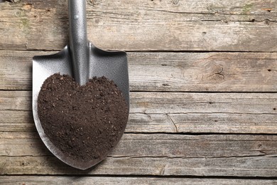 Photo of Metal shovel with soil on wooden table, top view. Space for text