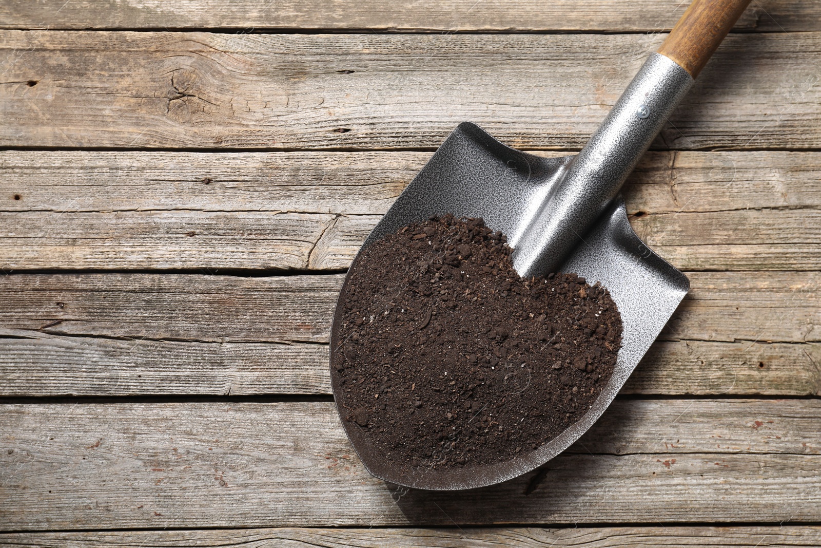 Photo of Metal shovel with soil on wooden table, top view. Space for text