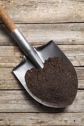 Photo of Metal shovel with soil on wooden table, top view