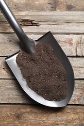 Photo of Metal shovel with soil on wooden table, top view