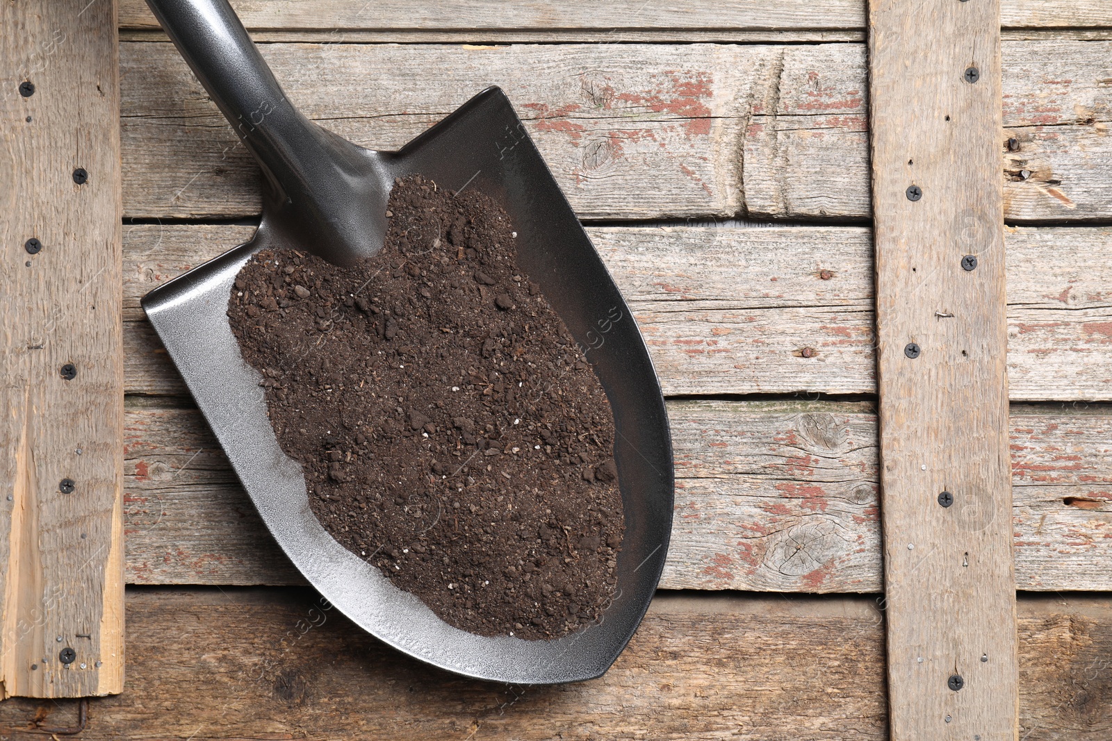 Photo of Metal shovel with soil on wooden table, top view. Space for text