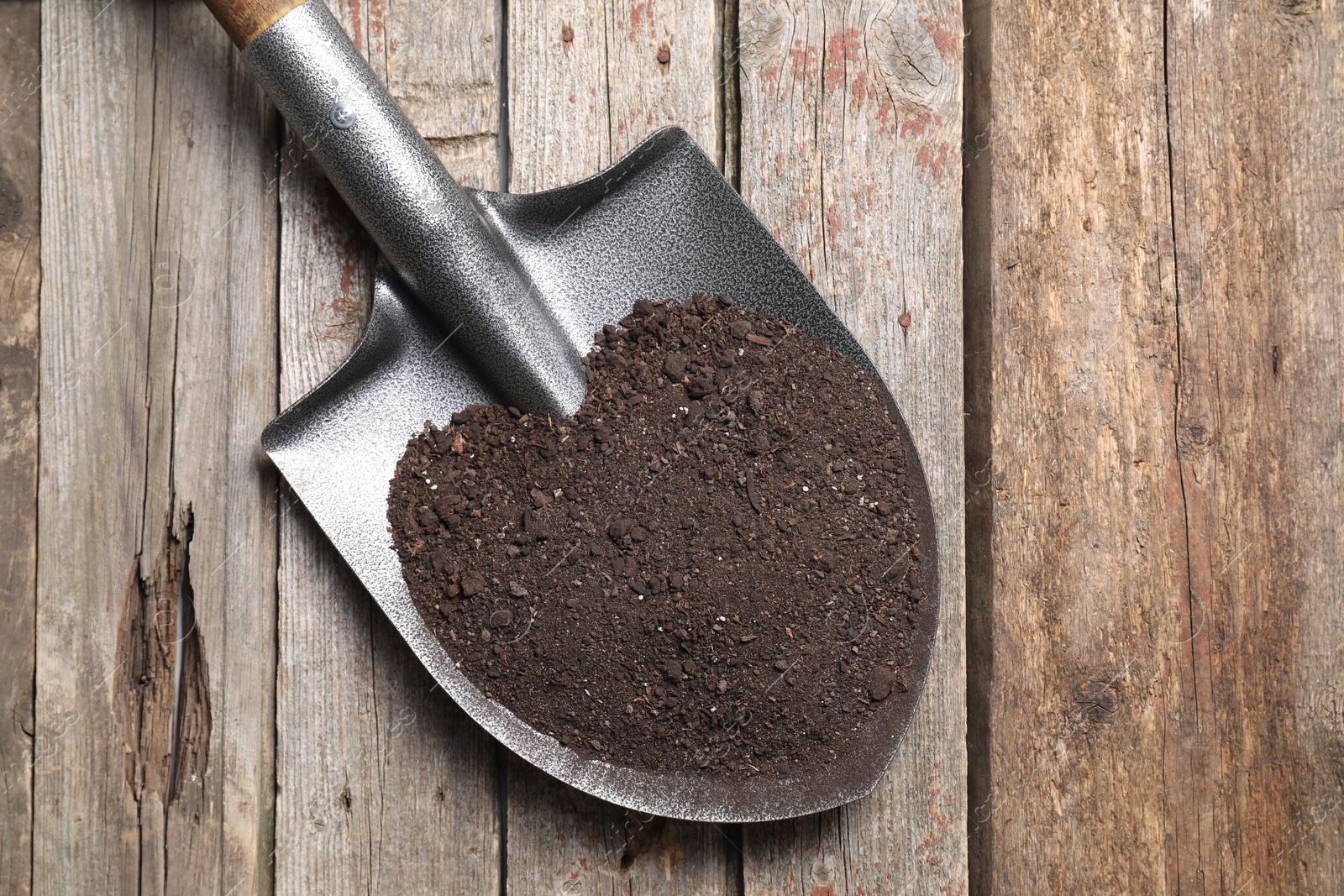 Photo of Metal shovel with soil on wooden table, top view