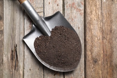 Photo of Metal shovel with soil on wooden table, top view