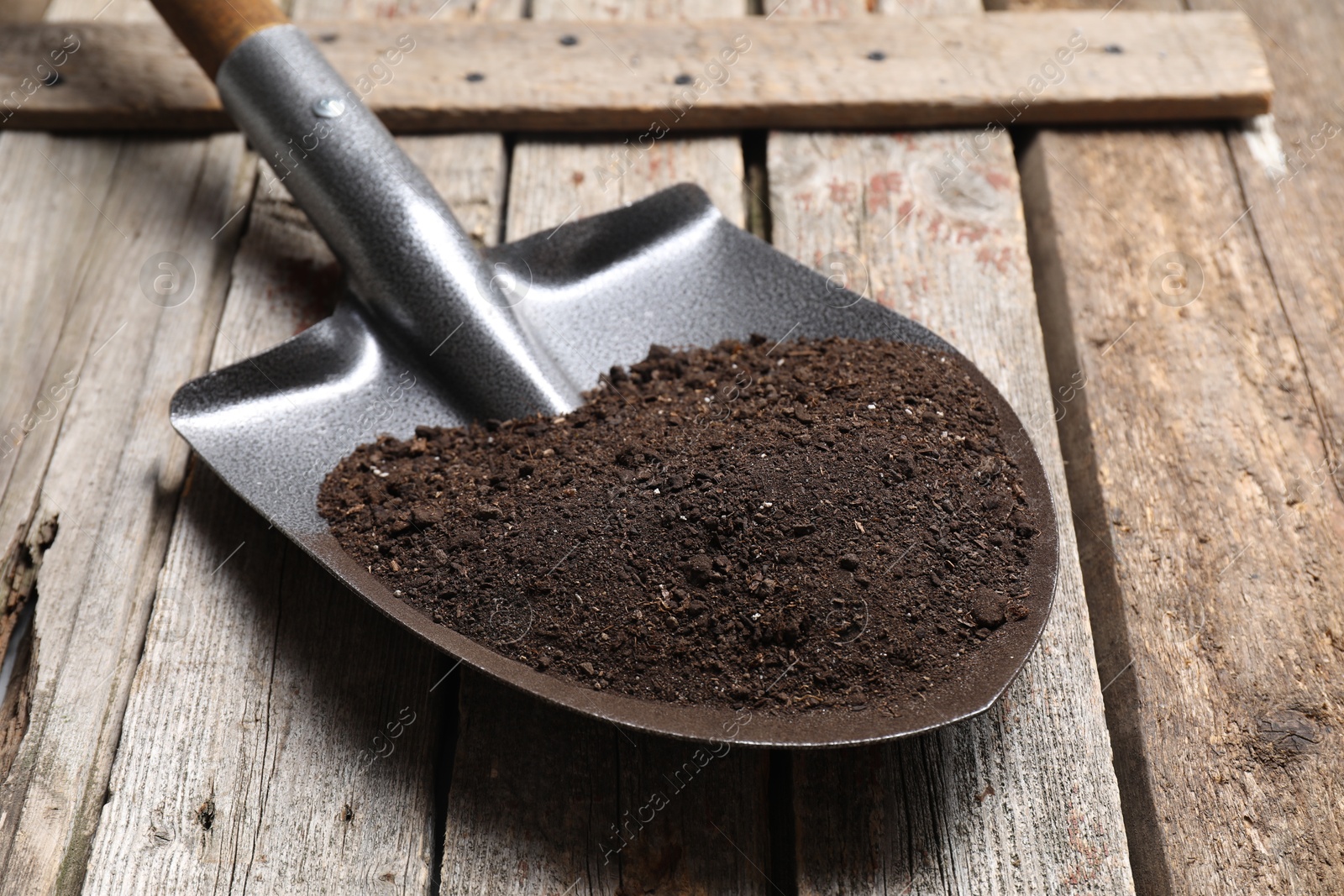 Photo of Metal shovel with soil on wooden table, closeup