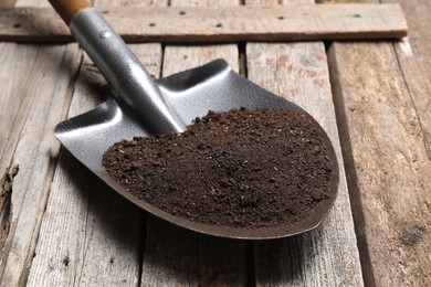 Photo of Metal shovel with soil on wooden table, closeup