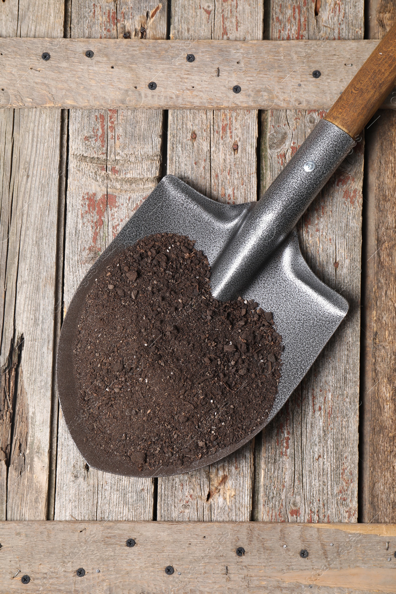 Photo of Metal shovel with soil on wooden table, top view