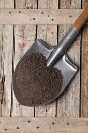 Photo of Metal shovel with soil on wooden table, top view