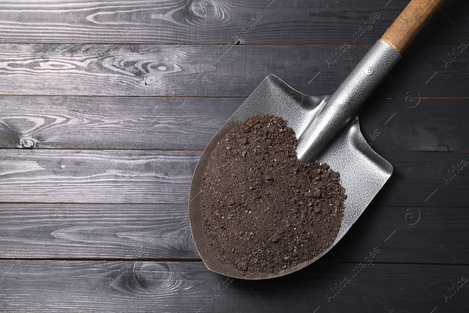 Photo of Metal shovel with soil on black wooden table, top view. Space for text