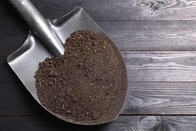 Photo of Metal shovel with soil on black wooden table, top view. Space for text