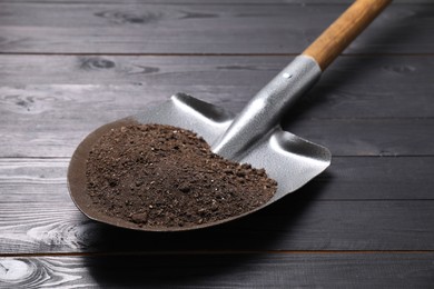 Photo of Metal shovel with soil on black wooden table, closeup