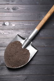 Photo of Metal shovel with soil on black wooden table, top view