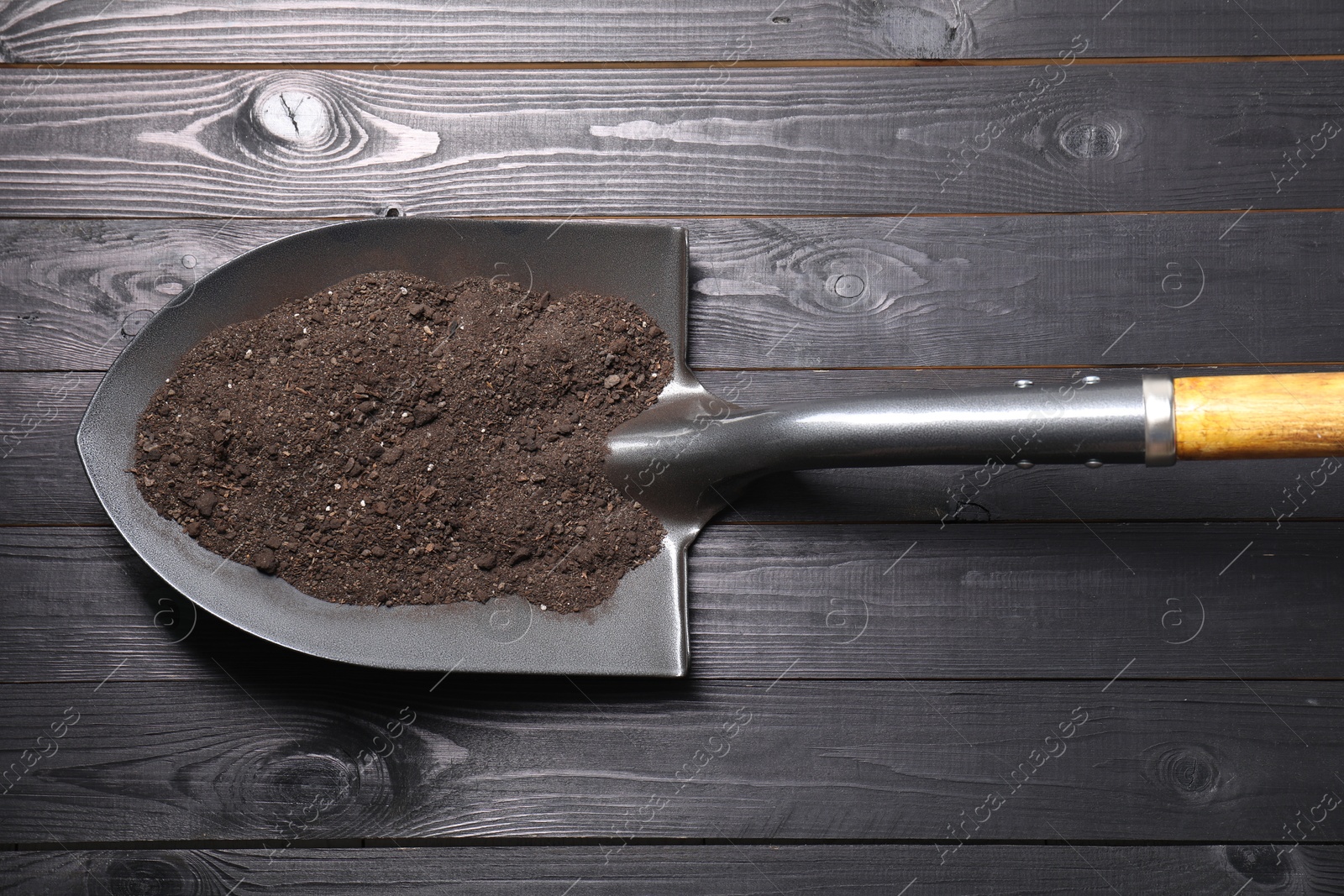 Photo of Metal shovel with soil on black wooden table, top view