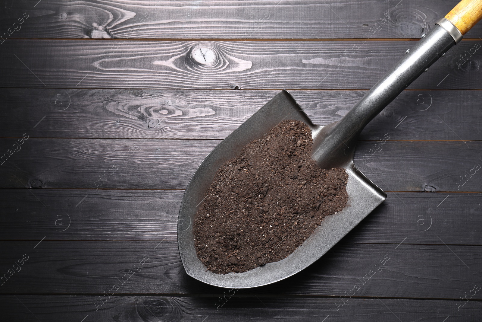 Photo of Metal shovel with soil on black wooden table, top view