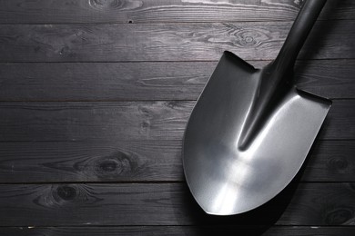 Photo of Metal shovel on black wooden table, top view. Space for text